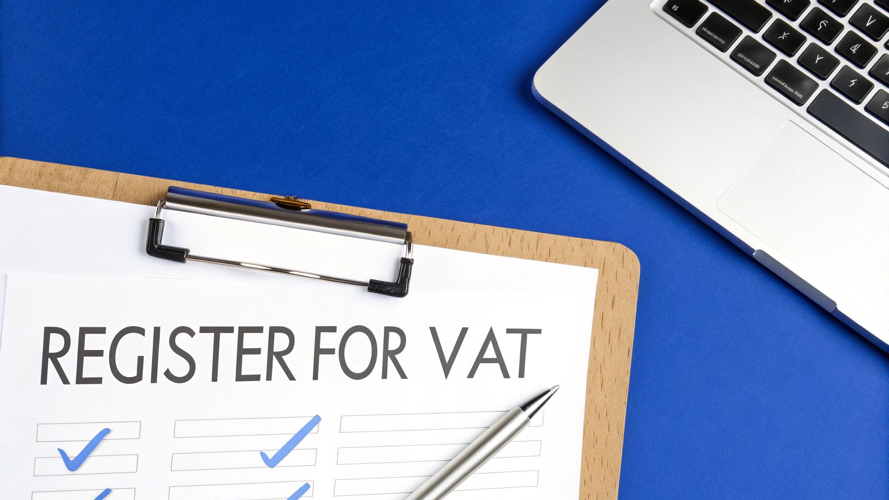 A person at a desk using a laptop with the HMRC logo on screen, surrounded by documents and a calculator, representing the VAT registration process.